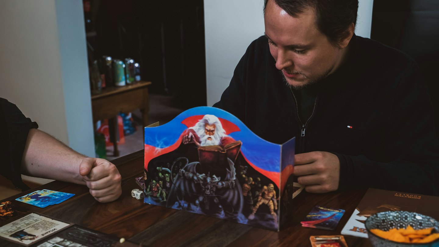 Man plays tabletop role-playing game with dice and character sheets.