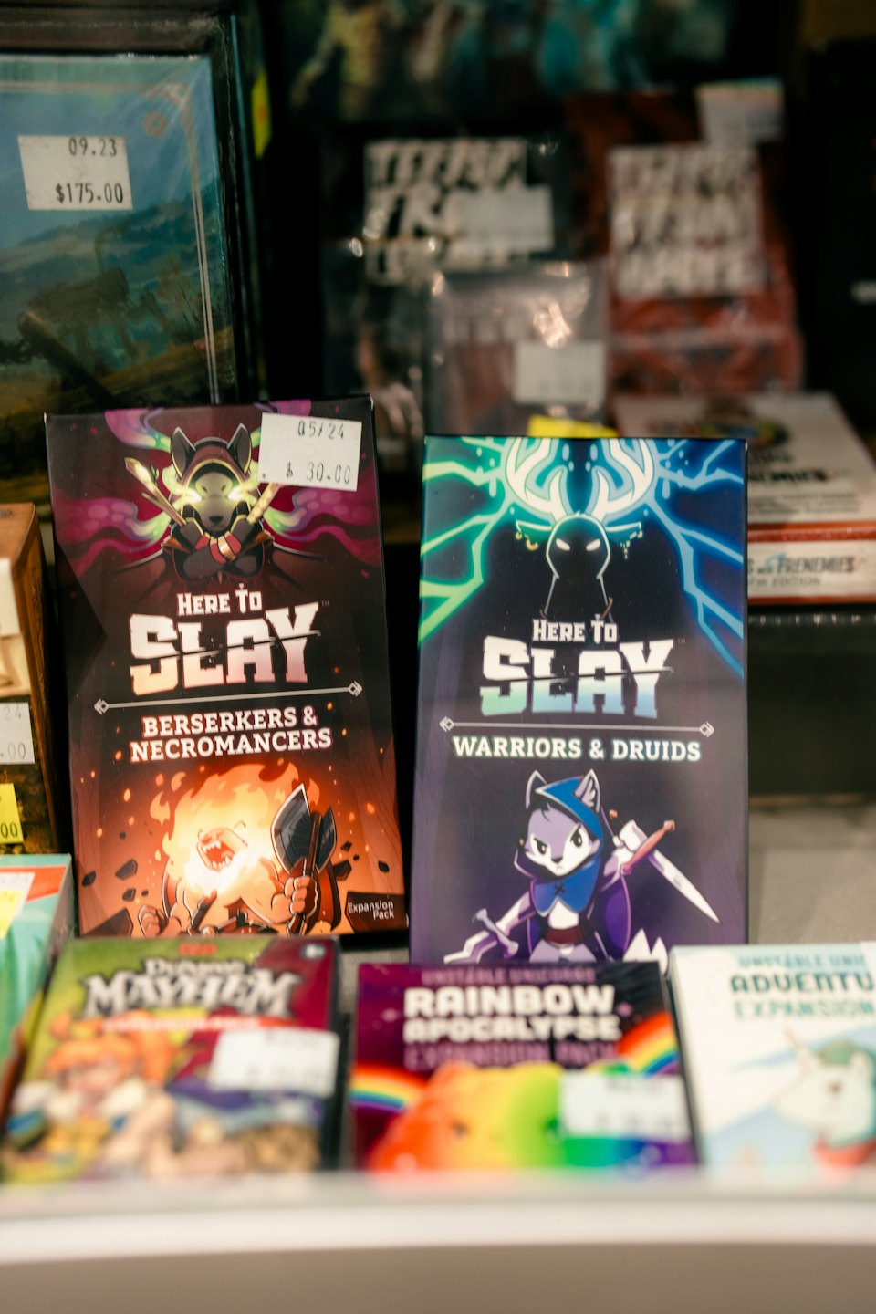 Board game boxes for Here to Slay displayed on shelves.