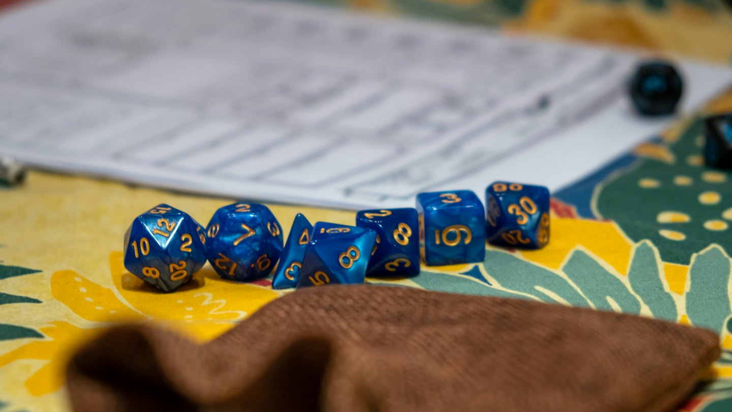 Blue and gold polyhedral dice on patterned fabric with character sheet.